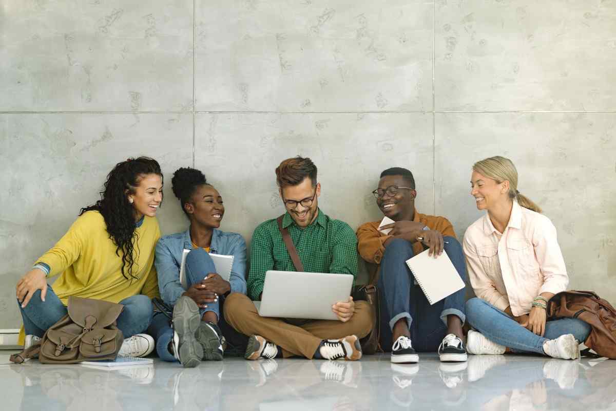 Happy university students using laptop while sitting in a hallway